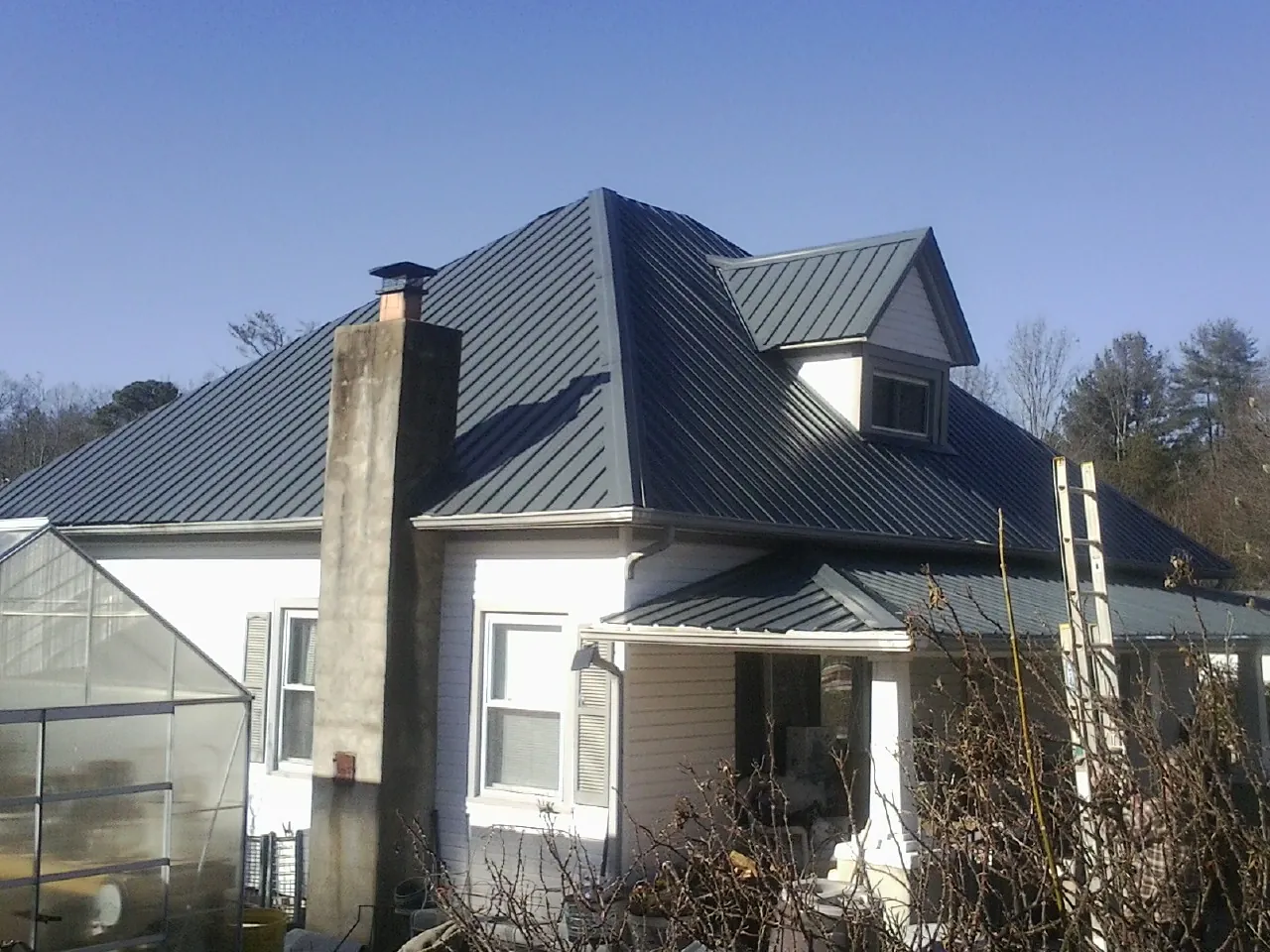 Dark blue standing seam metal roof on a white farmhouse with dormer — Slate & Tile Roof Repair by Roofing Brothers in Holder