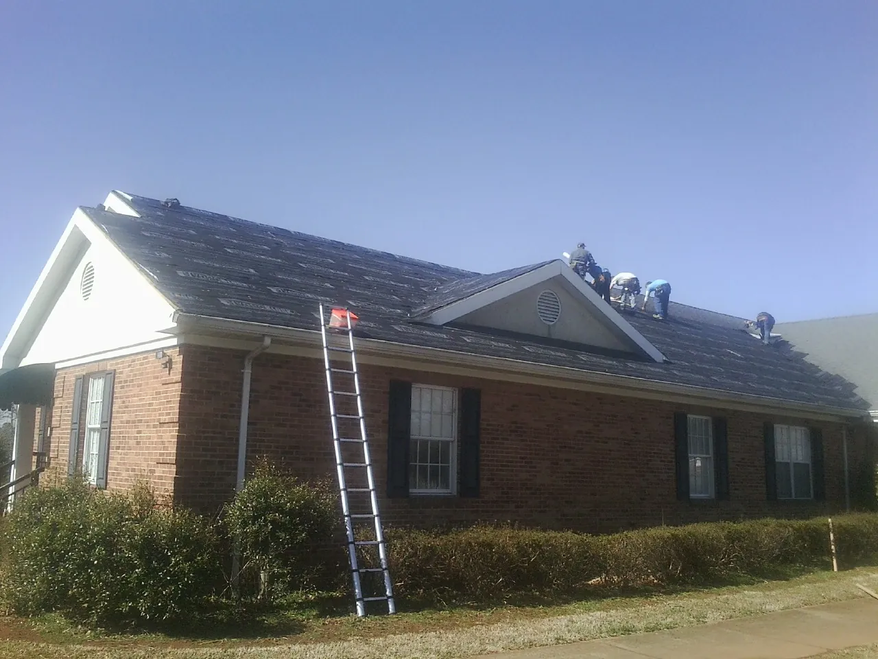Crew tearing shingles off a brick ranch roof with a ladder set — Emergency Roof Repair work by our crew in Holder