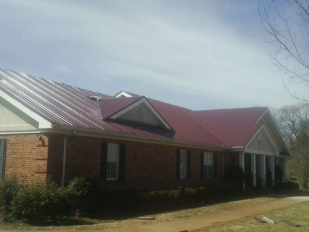 Red metal roof with gabled entries on a long brick building, from a Hail Damage Roof Repair job in Holder