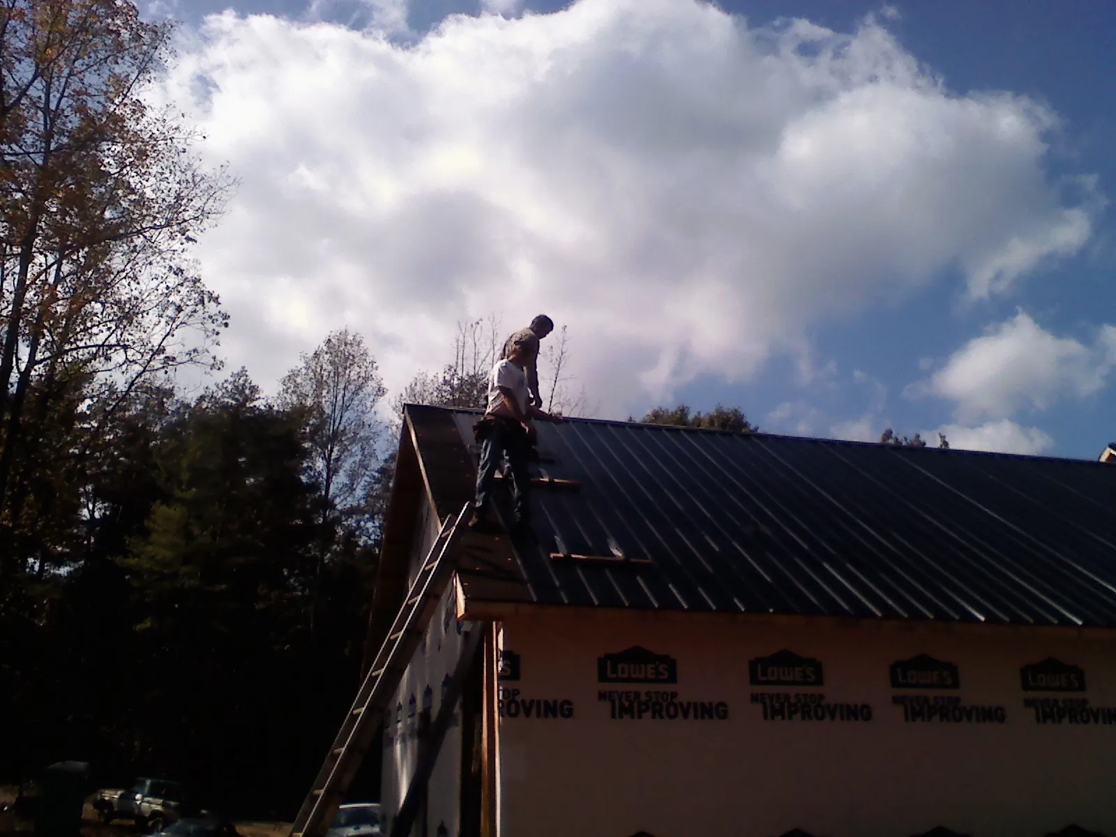 Roofer fastening dark metal panels high against a cloudy sky, from a Roof Inspection job in Holder