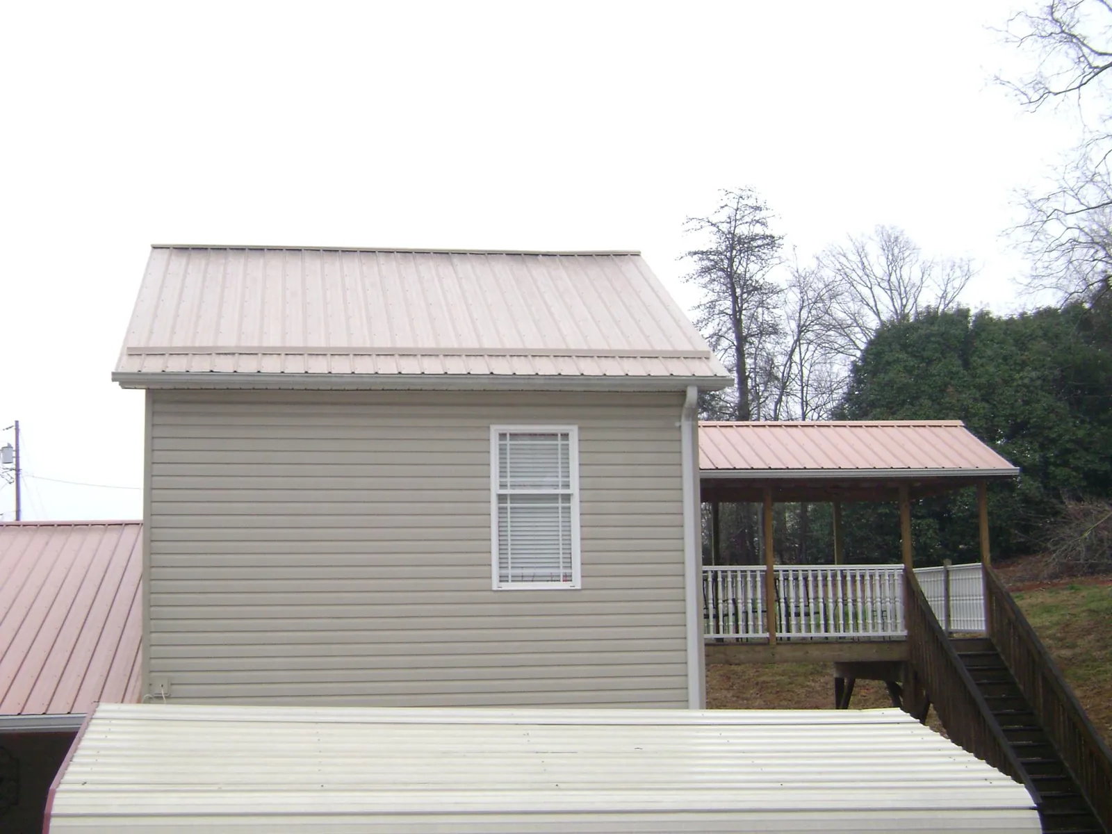 Tan metal roofs on a two story addition and attached porch, from a Roof Replacement job in Holder